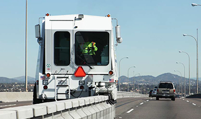 A barrier transfer machine or a zipper machine, also referred to as a road zipper is moving the divider eastbound on SR 75 or also known as the Coronado Bridge. There is some traffic in the background.