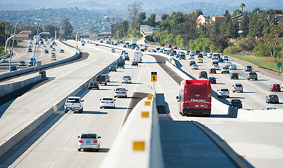 A MTS Rapid bus number 235 is traveling away, down a direct access ramp merging onto the separated express lanes, between north and southbound traffic on the I-15 freeway.
