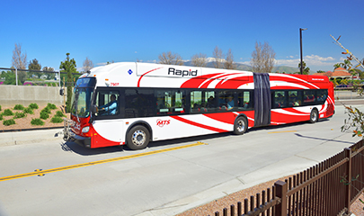 A red and white accordion Rapid bus with passengers on board is driving through a street with no traffic.