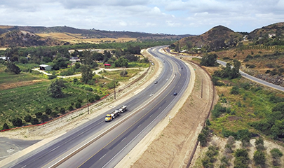 Aerial view of the SR 76 highway at a curved section showing a recently widen shoulder. The highway is located in a rural area with some hills and green vegetation.