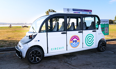 A 6-passenger white Circuit neighborhood electric vehicle is parked next to a park in Pacific Beach along Mission Bay.